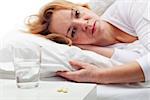 Taking pills - woman laying in bed with medication prepared on the night stand