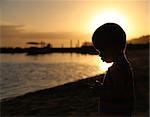 Silhouette of pensive little boy on the beach at sunset