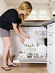 Photo of a blond female leaning over and unloading her dishwasher.