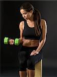 Photo of an attractive female doing a dumbbell curl while sitting.