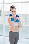 Cheerful athletic blonde exercising with dumbbells in bright room