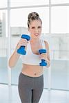 Competitive sporty blonde exercising with dumbbells in bright room