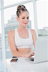 Happy athletic blonde typing on laptop in bright room