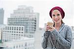Smiling casual blonde holding coffee outdoors on urban background