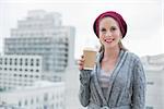 Cheerful casual blonde holding coffee outdoors on urban background