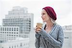 Thoughtful casual blonde holding coffee outdoors on urban background