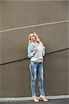 Thinking casual blonde wearing denim clothes posing outdoors against brown wall