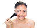 Delighted young dark haired model applying powder on her cheeks on white background