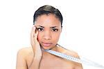 Worried young dark haired model holding measuring tape on white background