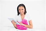 Pleased young dark haired model cuddling a pillow and using a tablet pc in bright bedroom