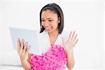 Cheerful young dark haired model chatting with tablet pc in bright bedroom