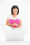 Concentrated young dark haired model cuddling a pillow and looking at a laptop in bright bedroom