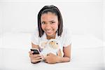 Charming young dark haired model holding a mobile phone and a plush sheep in bright bedroom