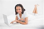 Pleased young dark haired model using a laptop in bright bedroom