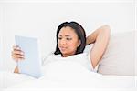 Relaxed young dark haired model using a tablet pc in bright bedroom