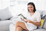 Pleased young dark haired woman in white clothes reading magazines in a living room