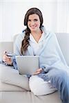 Charming casual brown haired woman in white pajamas shopping online with her tablet pc in a bright living room