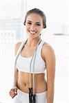 Cheerful sporty brunette wearing a skipping rope around the neck in bright room