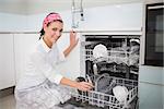 Cheerful charming woman using dish washer in bright kitchen