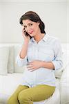 Content pregnant brown haired woman making a phone call in a bright living room
