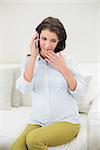 Attractive pregnant brown haired woman making a phone call in a bright living room