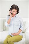 Peaceful pregnant brown haired woman making a phone call in a bright living room