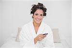 Smiling natural brunette holding smartphone in bedroom