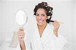 Cheerful natural brunette using brush and mirror in bedroom