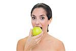 Smiling bare brunette eating green apple on white background