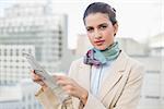 Serious smart brown haired businesswoman holding a newspaper outdoors