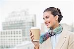 Happy smart brown haired businesswoman holding a cup of coffee outdoors