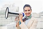 Happy smart brown haired businesswoman holding a megaphone outdoors