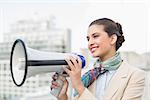 Pleased smart brown haired businesswoman holding a megaphone outdoors