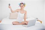 Relaxed natural brown haired woman in hair curlers shopping online with a laptop in bright bedroom