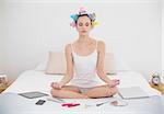 Peaceful natural brown haired woman in hair curlers meditating in lotus position in bright bedroom