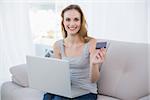 Happy young woman sitting on couch using laptop for online shopping at home in the living room