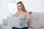 Young woman sitting on couch using laptop for online shopping at home in the living room