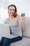 Laughing young woman sitting on couch using laptop for shopping online at home in the living room