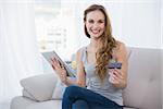 Happy young woman sitting on couch using tablet for shopping online at home in the living room