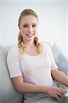 Casual cheerful blonde sitting on couch using laptop in bright living room