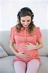 Gorgeous pregnant woman listening to music sitting in the living room at home