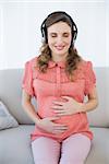 Pregnant woman relaxing sitting on couch with closed eyes while listening to music