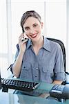 Friendly businesswoman phoning with her smartphone sitting at her desk