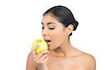 Calm nude brunette eating green apple on white background