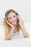 Pretty happy blonde lying on bed phoning in bright bedroom