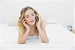 Pretty content blonde lying on bed phoning in bright bedroom