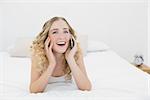 Pretty cheerful blonde lying on bed phoning in bright bedroom