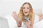 Pretty waving blonde lying on bed using laptop for online shopping in bright bedroom