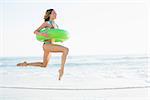 Beautiful young woman holding a rubber ring jumping on the beach