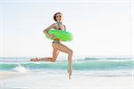 Gorgeous young woman holding a rubber ring while jumping on beach and looking at camera